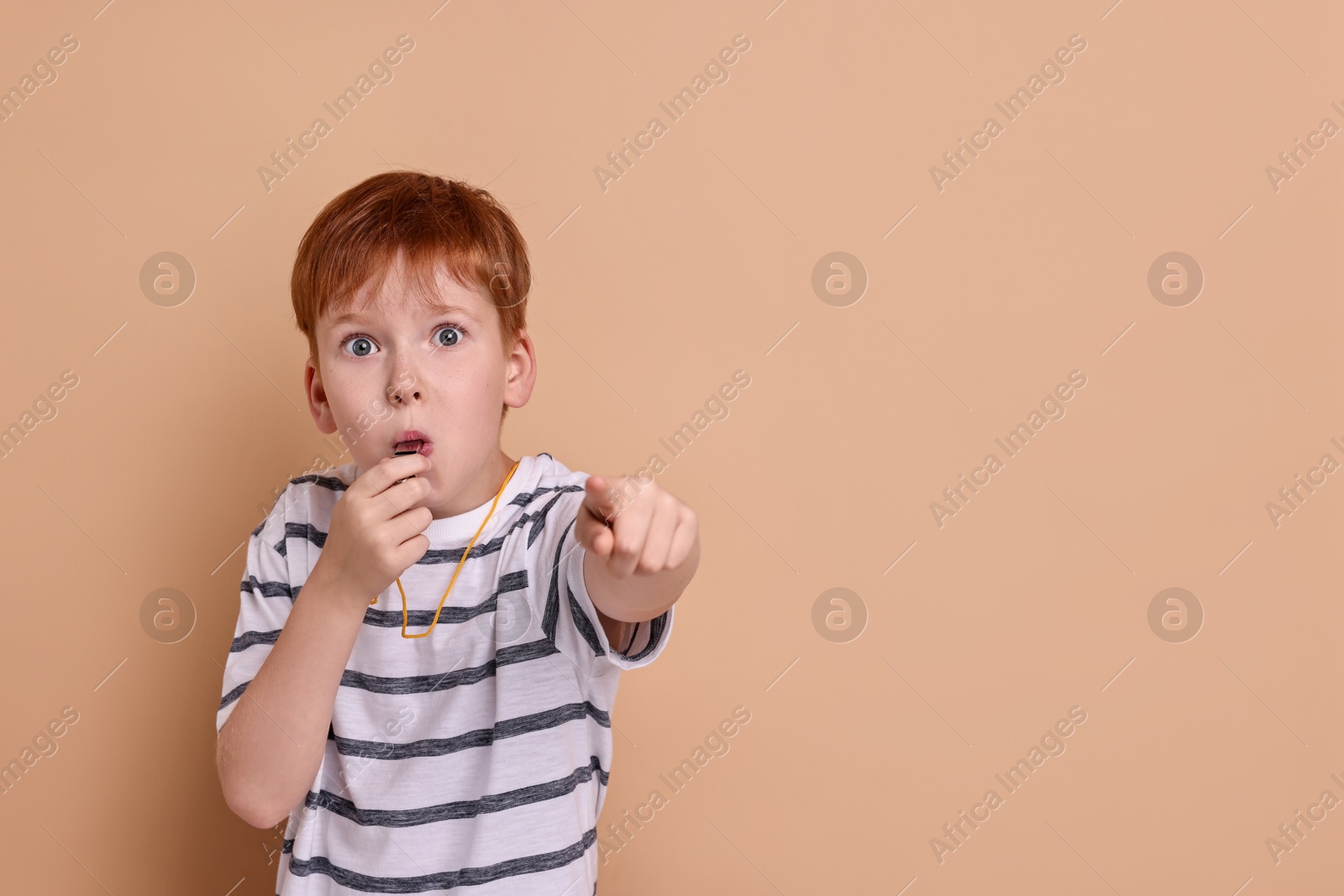 Photo of Little boy blowing whistle on beige background, space for text