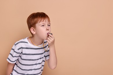 Photo of Little boy blowing whistle on beige background, space for text