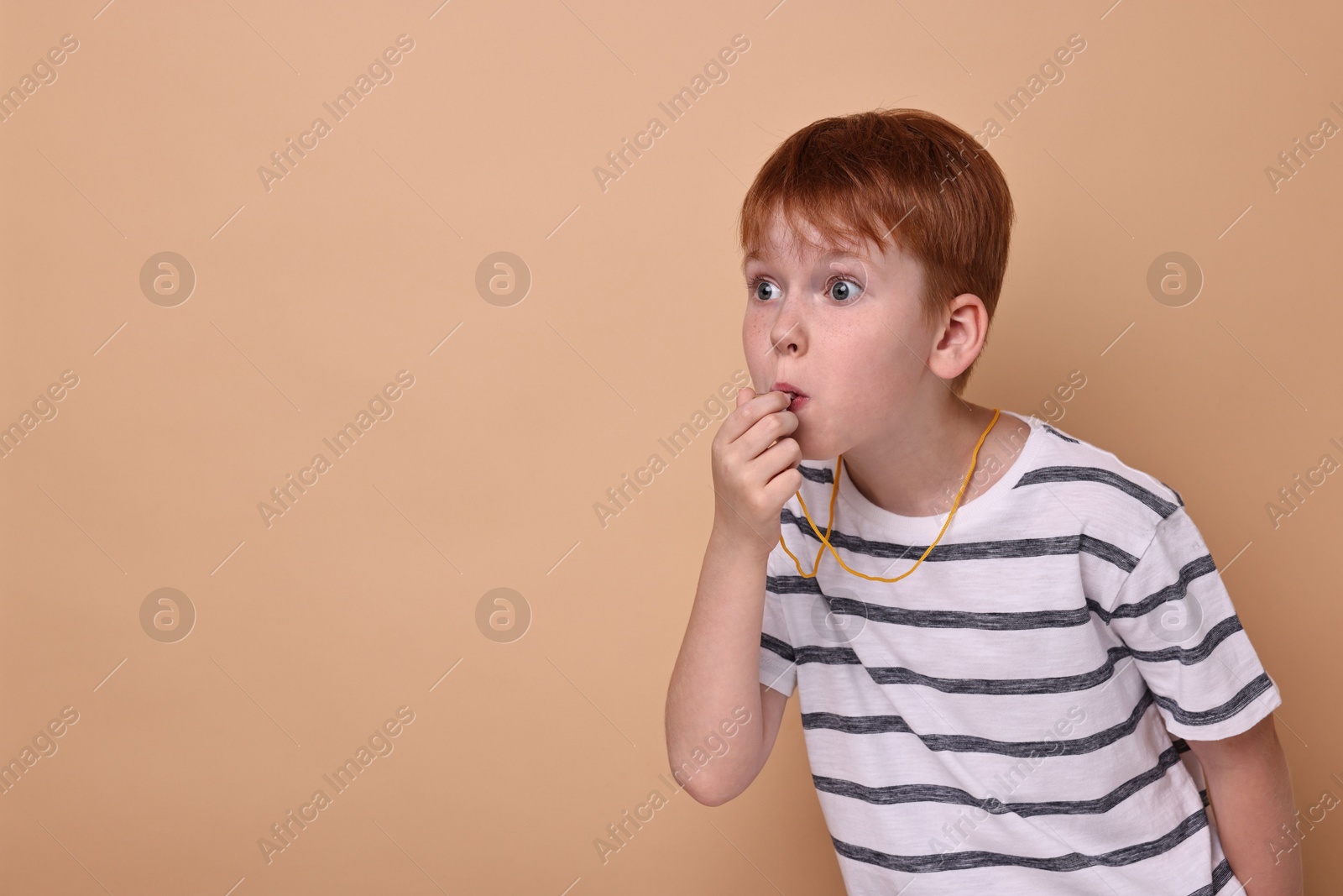 Photo of Little boy blowing whistle on beige background, space for text