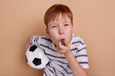 Little boy with soccer ball blowing whistle on beige background