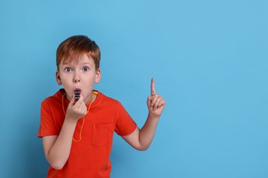 Photo of Little boy blowing whistle on light blue background, space for text