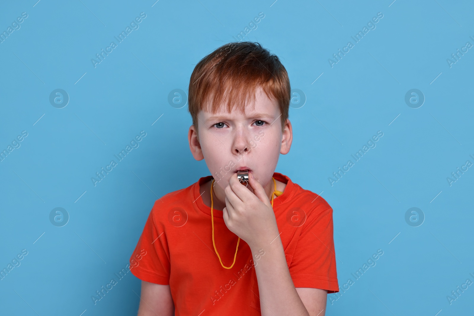 Photo of Little boy blowing whistle on light blue background