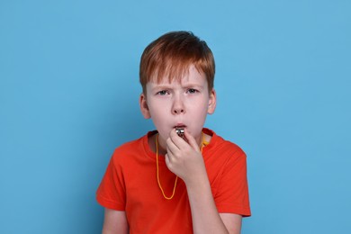 Photo of Little boy blowing whistle on light blue background