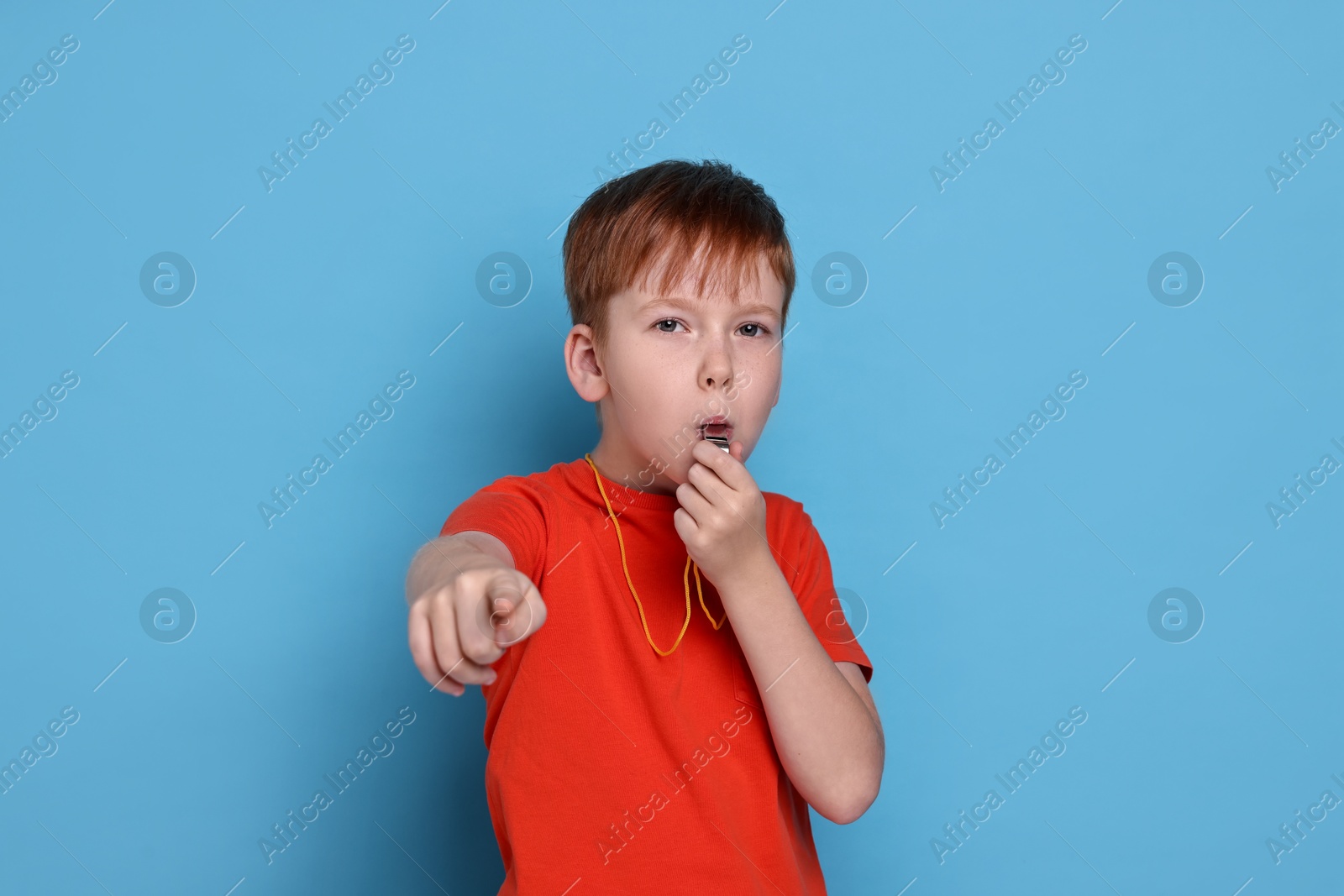 Photo of Little boy blowing whistle on light blue background