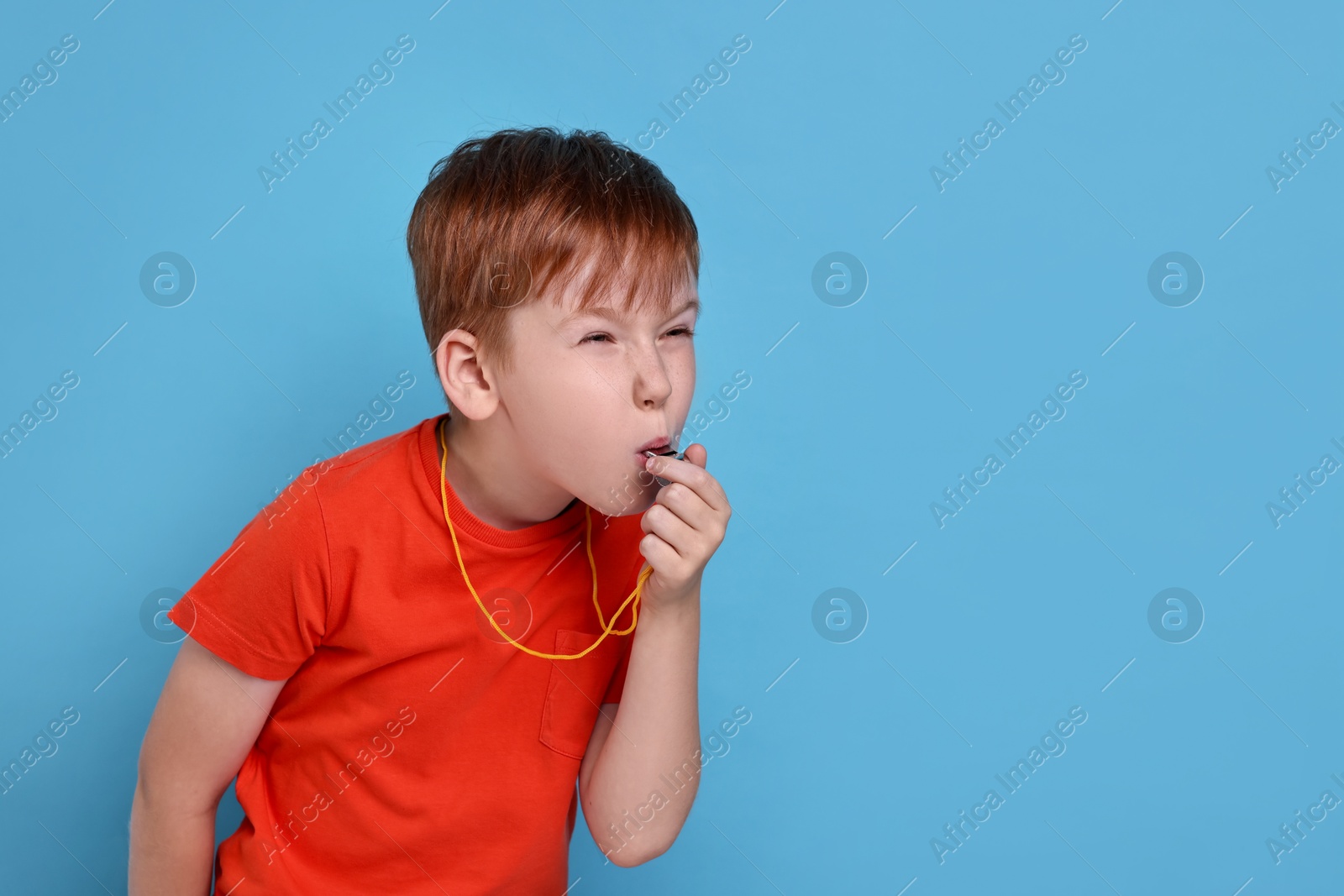 Photo of Little boy blowing whistle on light blue background, space for text