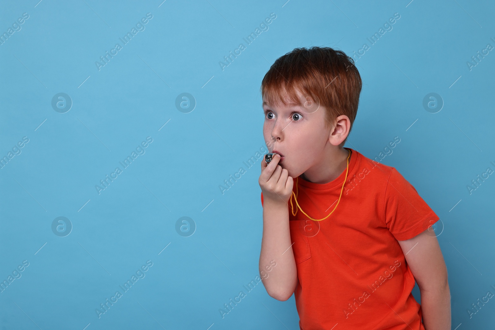 Photo of Little boy blowing whistle on light blue background, space for text