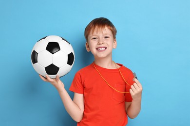 Photo of Little boy with whistle and soccer ball on light blue background