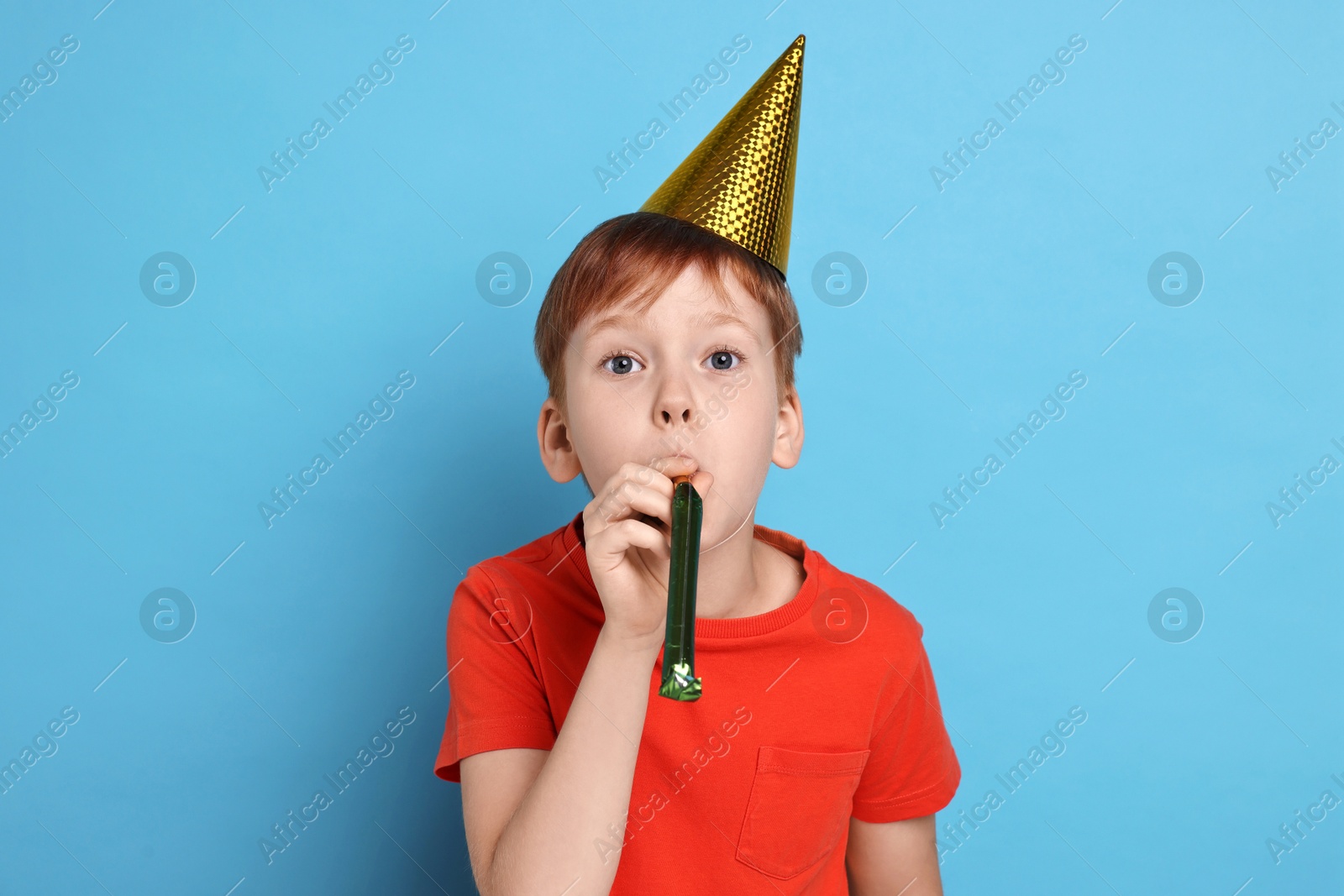 Photo of Little boy in party hat with blower on light blue background