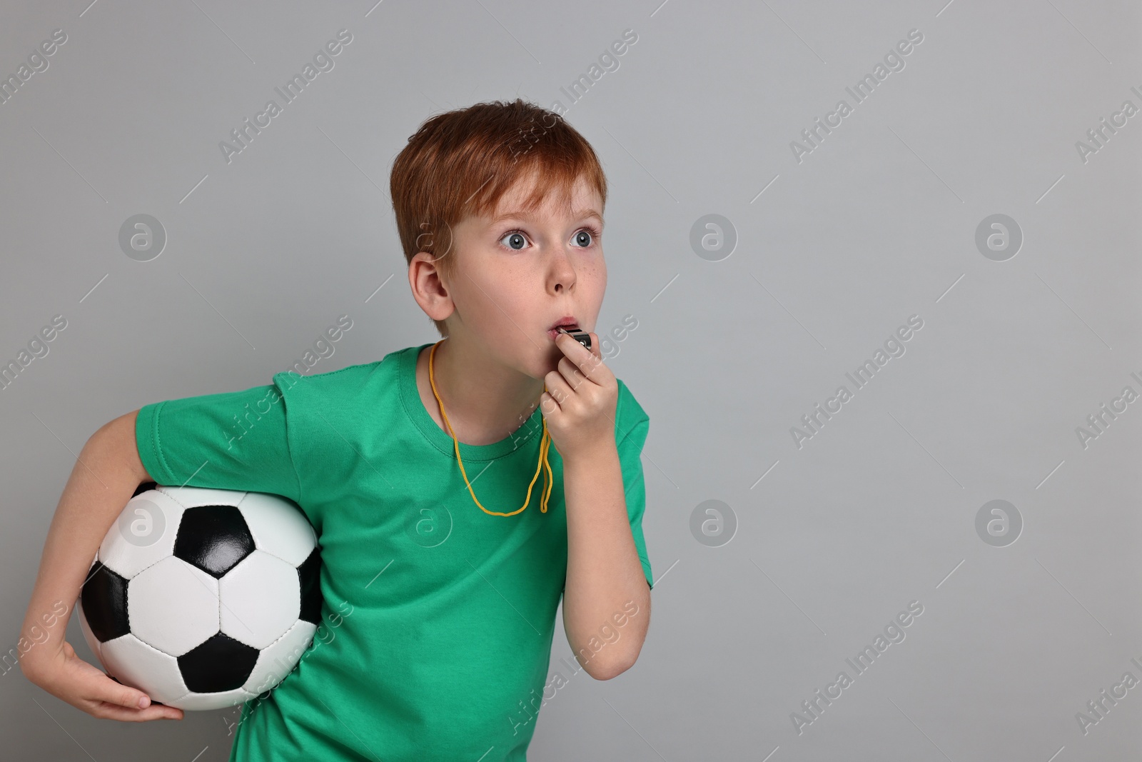 Photo of Little boy with soccer ball blowing whistle on grey background, space for text