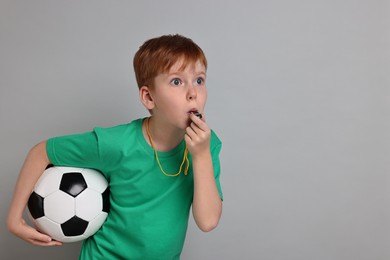 Little boy with soccer ball blowing whistle on grey background, space for text