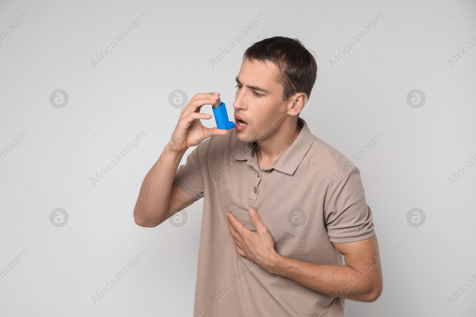 Photo of Man using asthma inhaler on light background