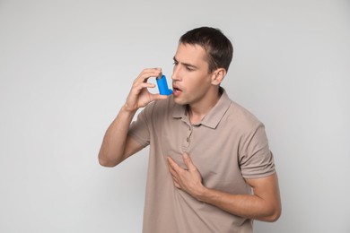 Photo of Man using asthma inhaler on light background