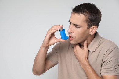 Photo of Man using asthma inhaler on light background