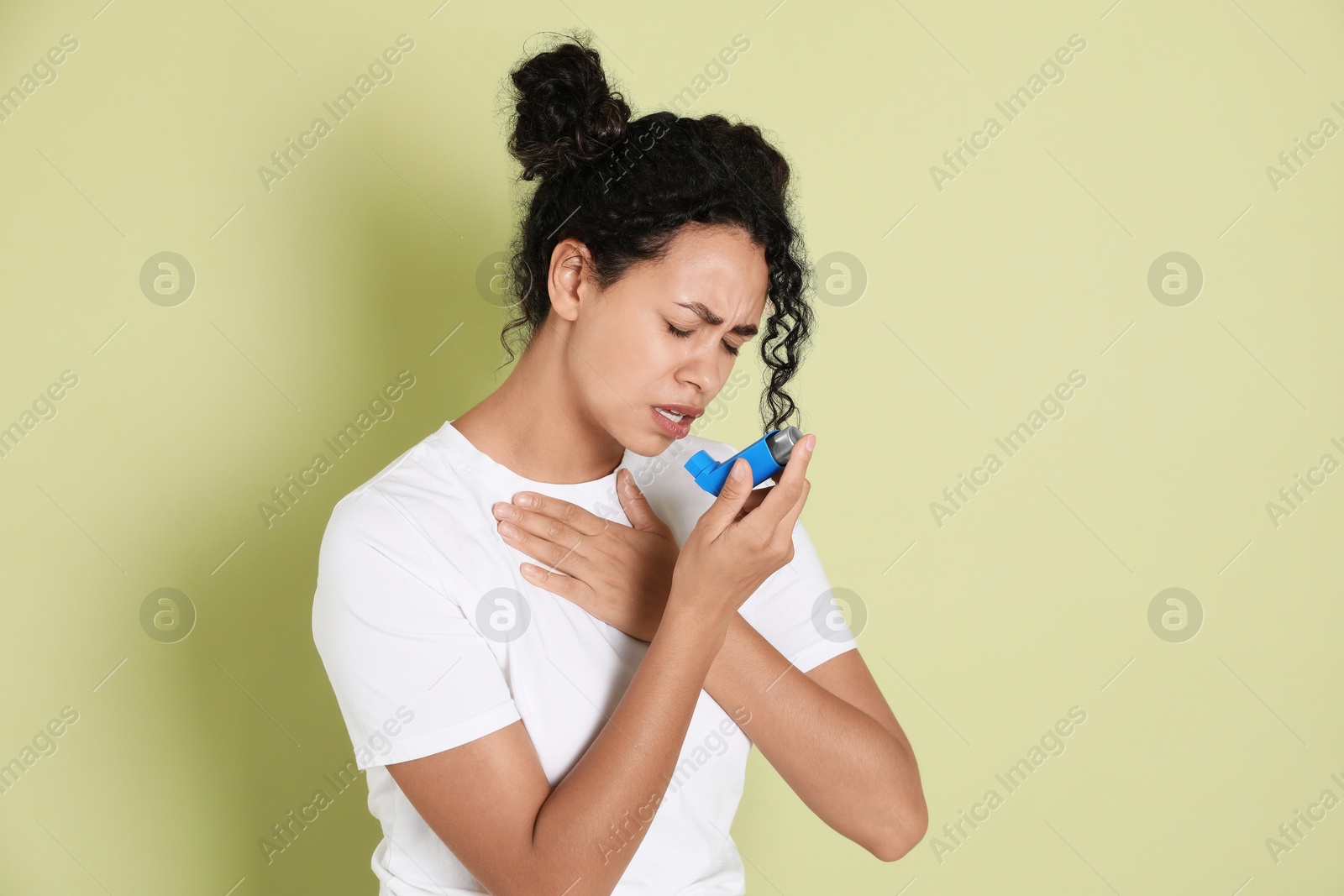 Photo of Young woman using asthma inhaler on light green background