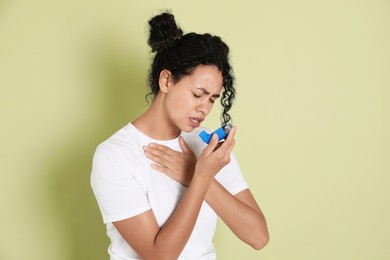 Photo of Young woman using asthma inhaler on light green background