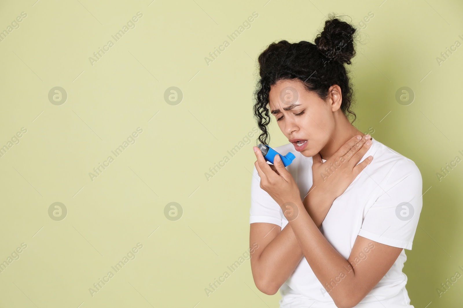 Photo of Young woman using asthma inhaler on light green background. Space for text