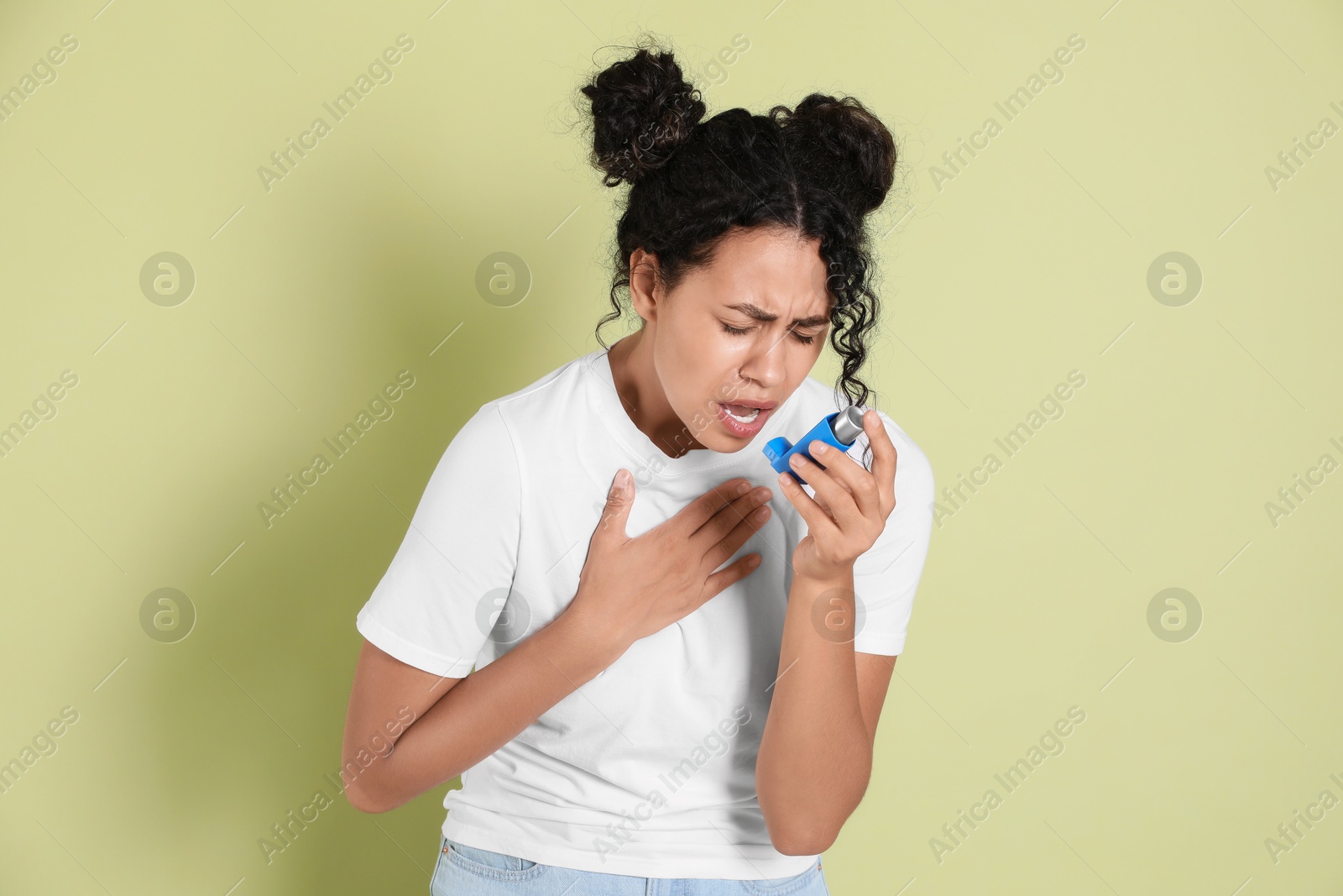 Photo of Young woman using asthma inhaler on light green background