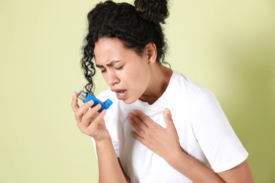 Photo of Young woman using asthma inhaler on light green background