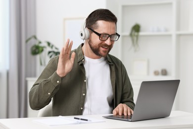 Interpreter in headphones having video chat via laptop at white table indoors