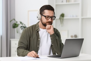 Photo of Interpreter in headphones having video chat via laptop at white table indoors