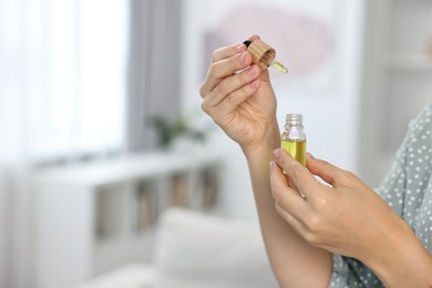 Young woman taking CBD tincture indoors, closeup. Space for text