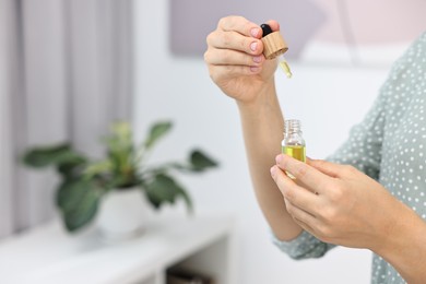 Photo of Young woman taking CBD tincture indoors, closeup. Space for text