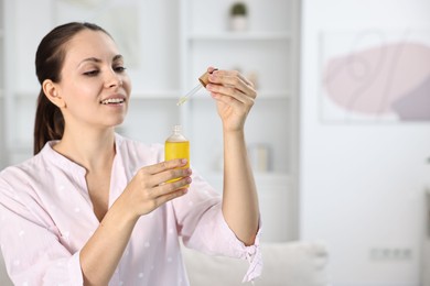 Photo of Young woman taking CBD tincture indoors, space for text