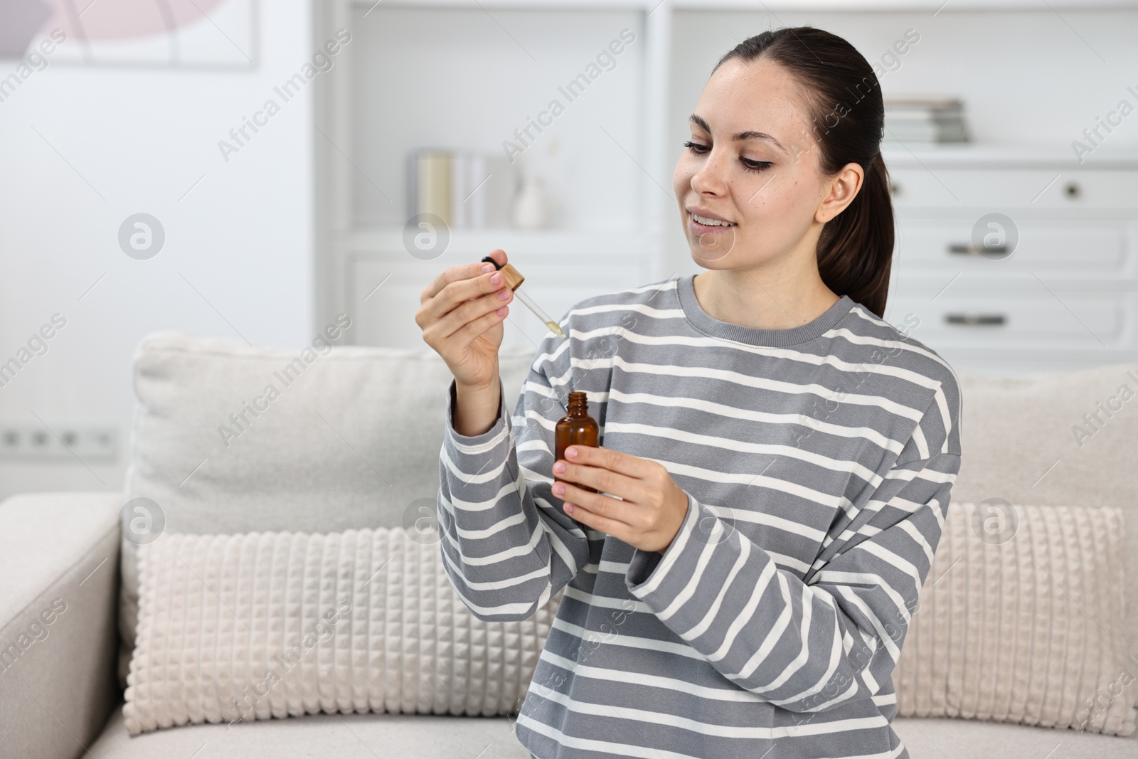 Photo of Young woman taking CBD tincture indoors, space for text