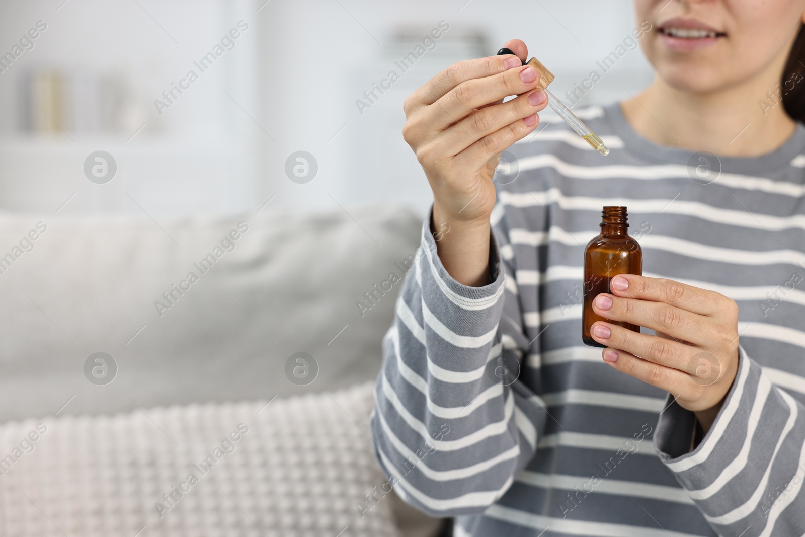 Photo of Young woman taking CBD tincture indoors, closeup. Space for text