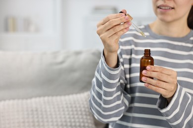 Photo of Young woman taking CBD tincture indoors, closeup. Space for text