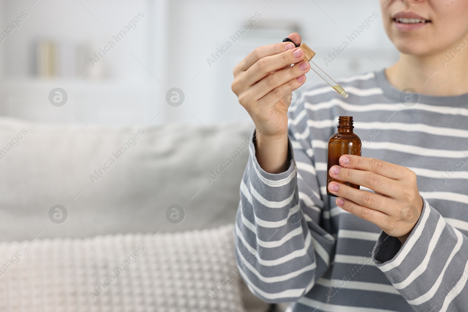 Photo of Young woman taking CBD tincture indoors, closeup. Space for text