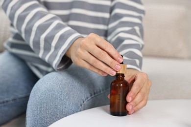 Young woman taking CBD tincture at white table, closeup