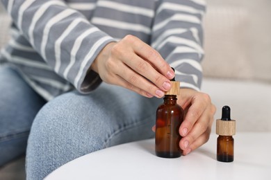 Photo of Young woman taking CBD tincture at white table, closeup