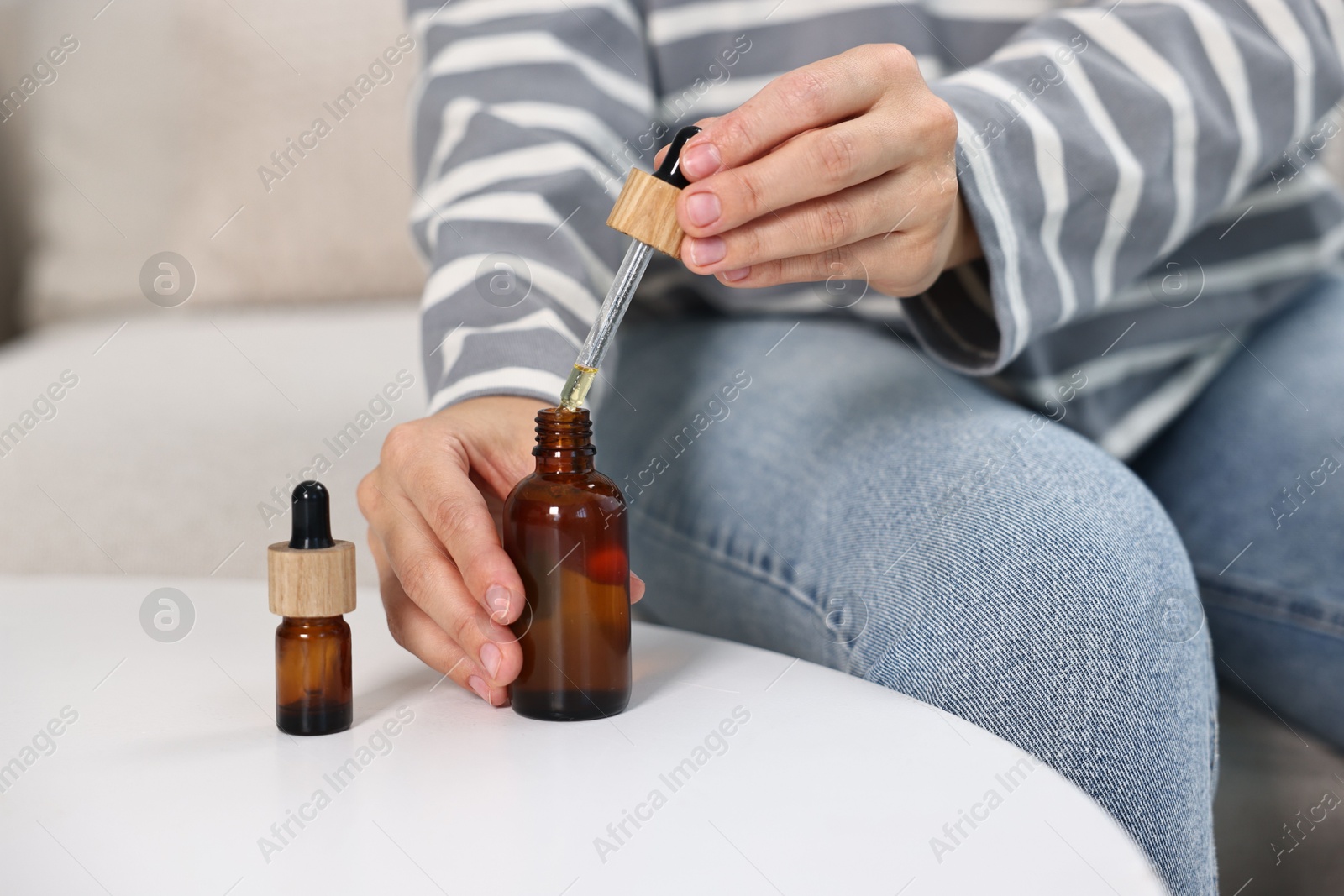 Photo of Young woman taking CBD tincture at white table, closeup