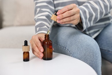 Young woman taking CBD tincture at white table, closeup