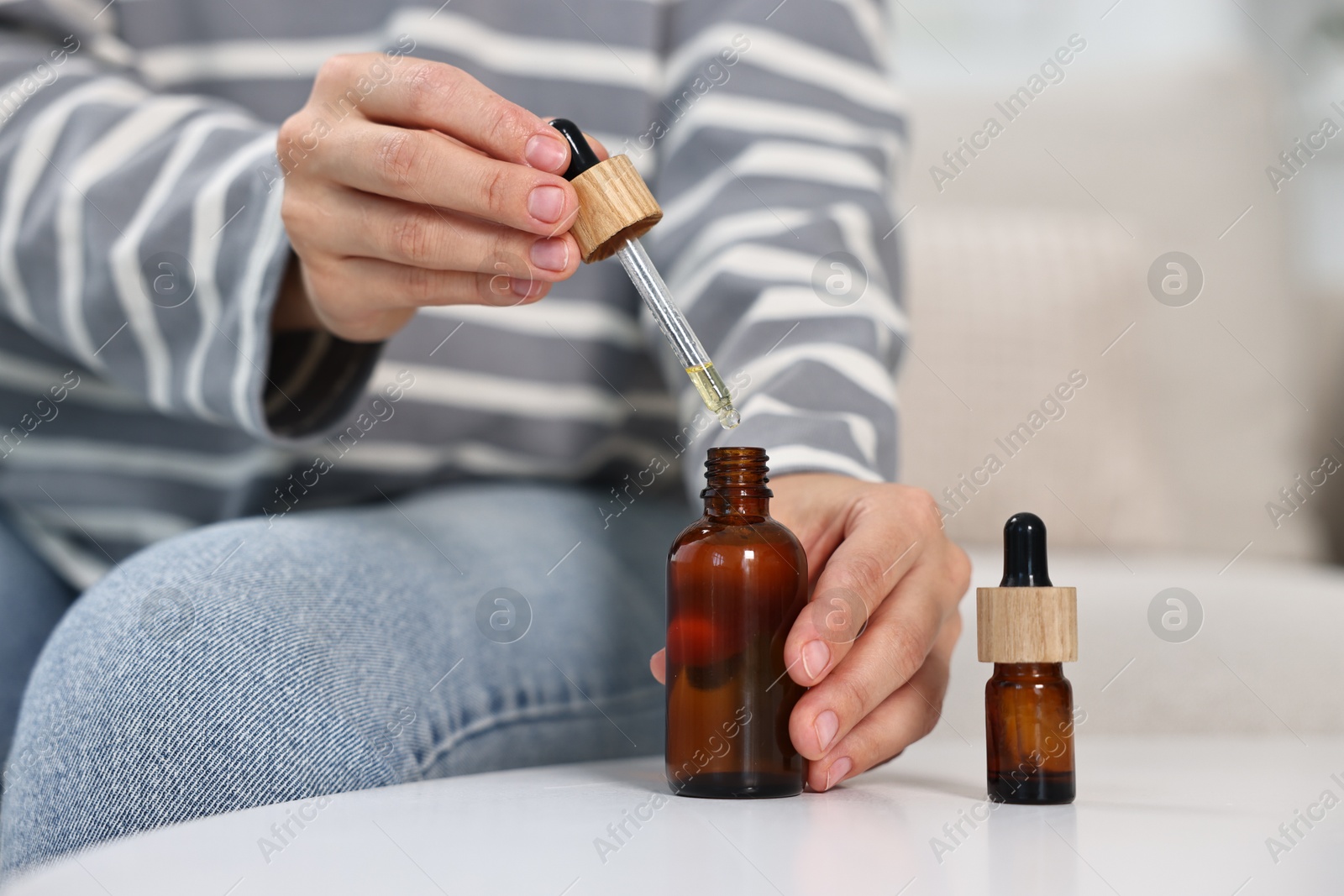 Photo of Young woman taking CBD tincture at white table, closeup