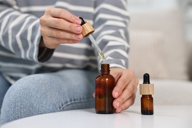 Young woman taking CBD tincture at white table, closeup