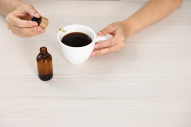 Young woman putting CBD tincture into cup with drink at white wooden table, closeup. Space for text