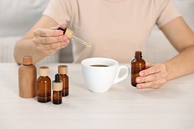 Photo of Young woman putting CBD tincture into cup with drink at white wooden table, closeup