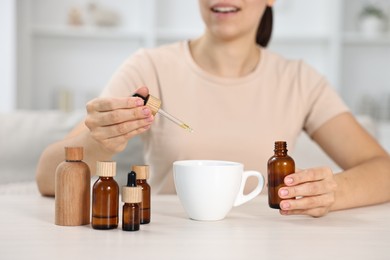 Photo of Young woman putting CBD tincture into cup with drink at white wooden table, closeup