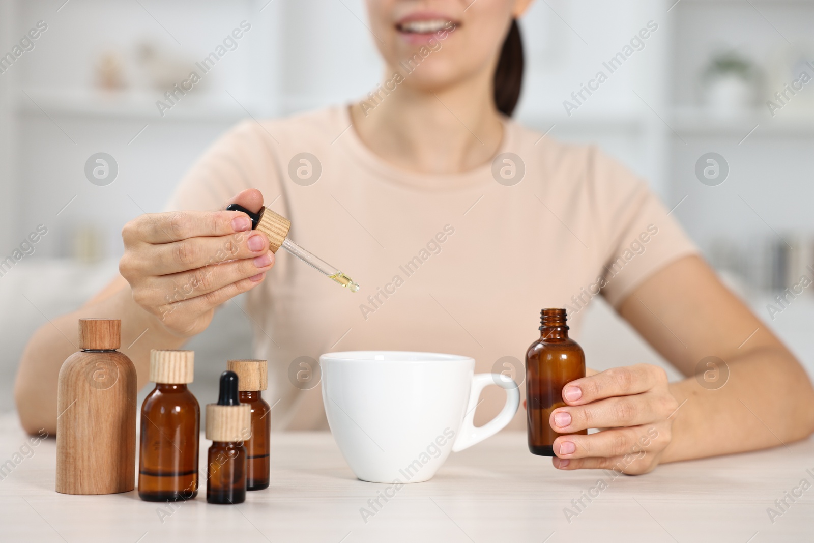 Photo of Young woman putting CBD tincture into cup with drink at white wooden table, closeup