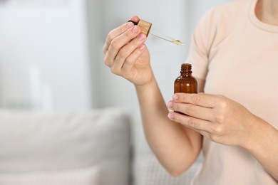 Photo of Young woman taking CBD tincture indoors, closeup. Space for text