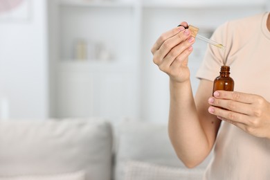 Young woman taking CBD tincture indoors, closeup. Space for text