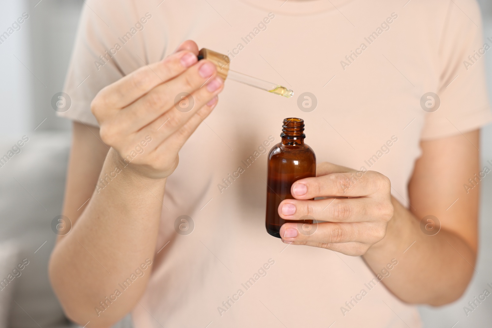 Photo of Young woman taking CBD tincture indoors, closeup