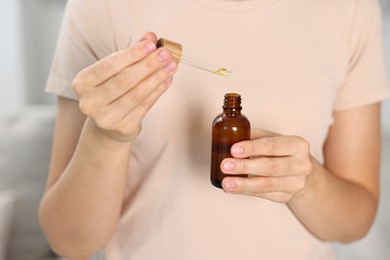 Young woman taking CBD tincture indoors, closeup