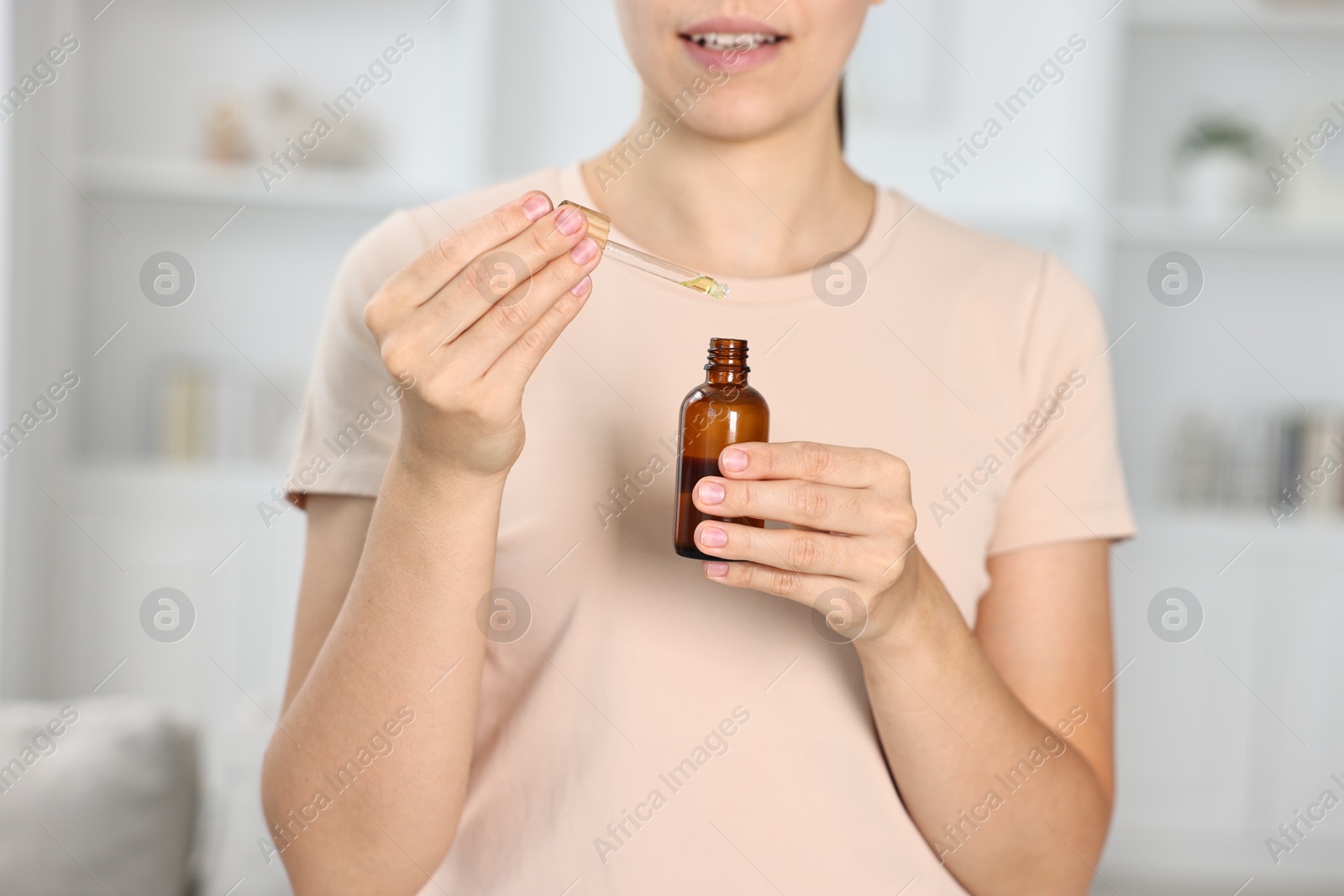 Photo of Young woman taking CBD tincture indoors, closeup