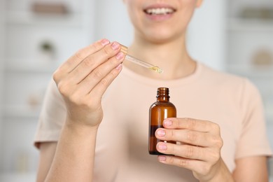 Young woman taking CBD tincture indoors, closeup