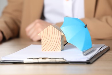 Photo of Property insurance. Real estate agent working at table indoors, focus on wooden house figure and small umbrella