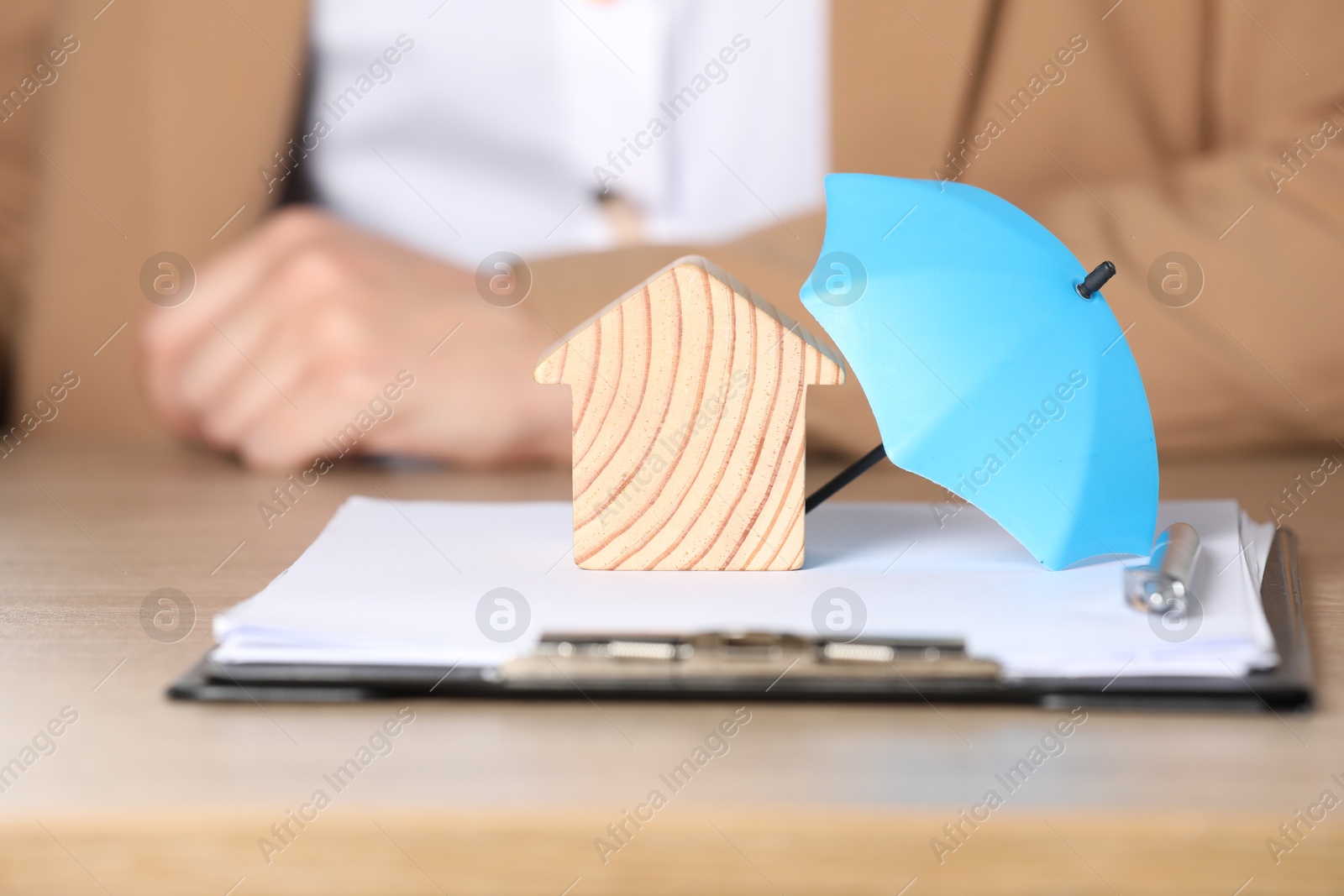 Photo of Property insurance. Real estate agent working at table indoors, focus on wooden house figure and small umbrella