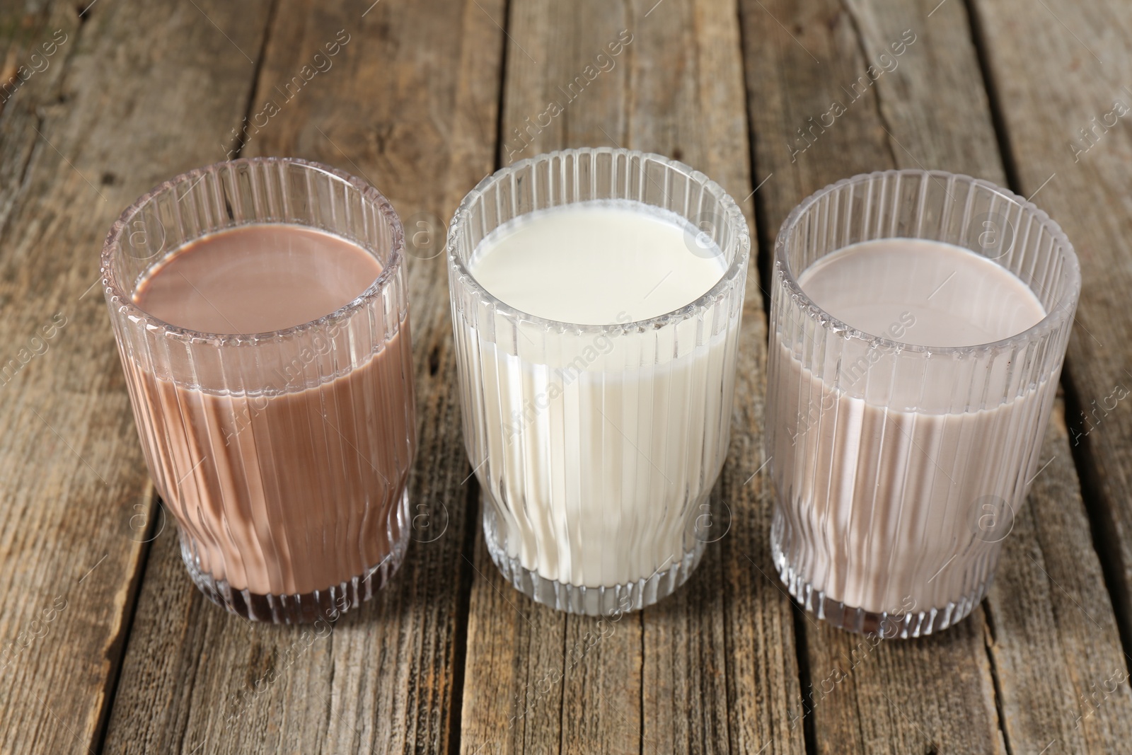 Photo of Different tasty protein cocktails in glasses on wooden table